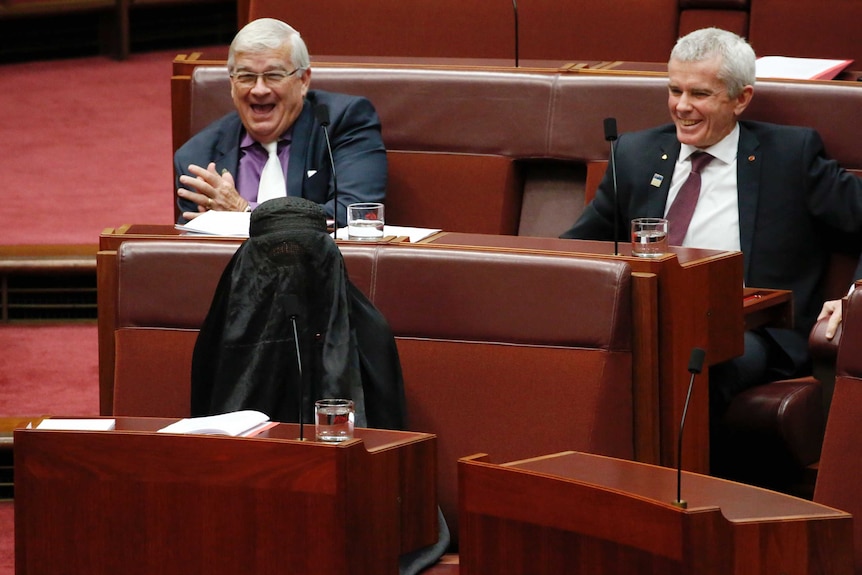 Pauline Hanson in burqa, Malcolm Roberts and Brian Burston laugh in background