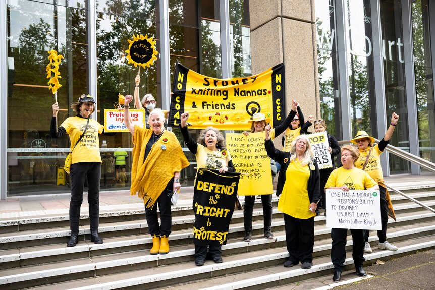 A group of women wearing bright yellow, hold signs like 'defend the right to protest' outside the NSW Supreme Court. 