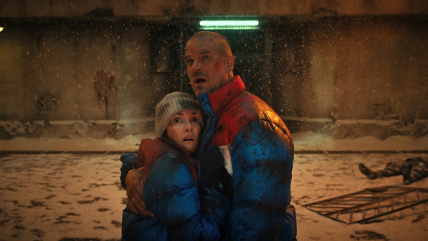 A bloody and brusied couple embrace in a snowy prison courtyard