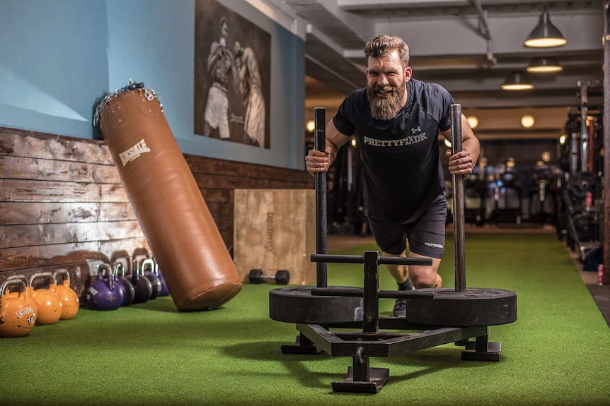 Muscular man working out on a machine in the gym for a story about not using towels to wipe down gym equipment.