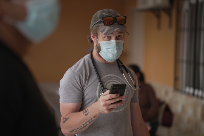A man wearing a medical mask and t-shirt has stethoscope around his neck.