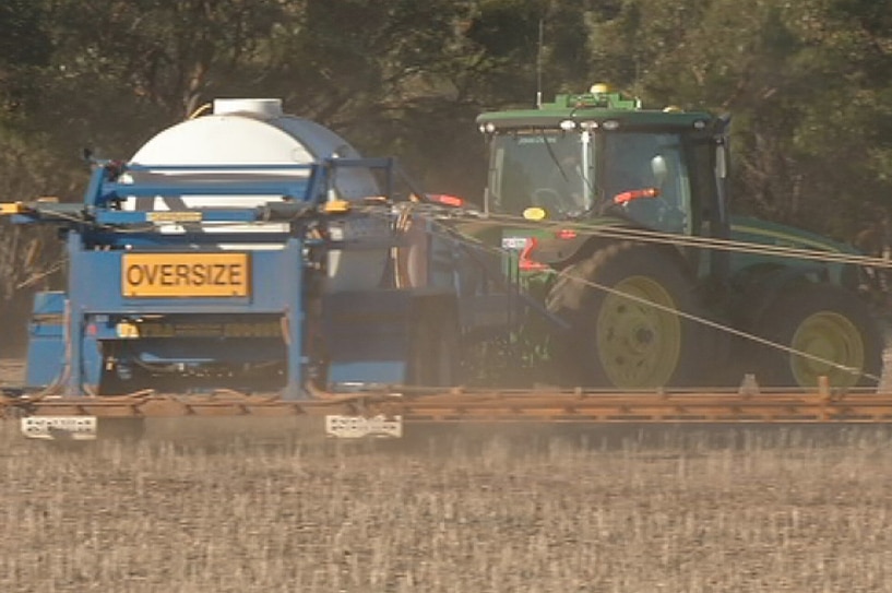 A tractor pulls a seeder through a dusty field