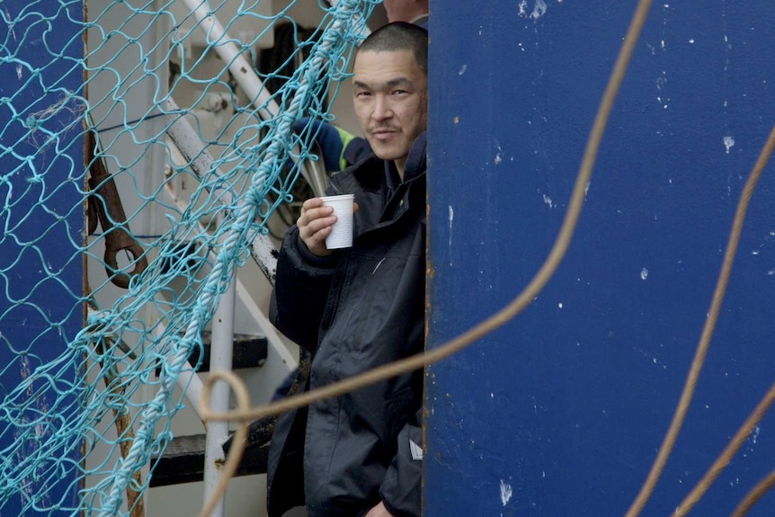 A man leans against a wall holding a cup