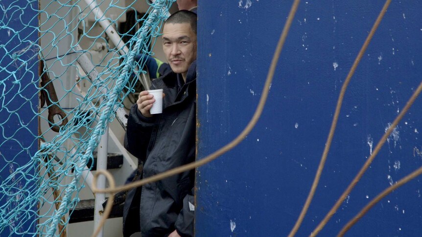 A man leans against a wall holding a cup