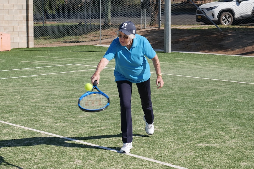 An elderly woman hitting a tennis ball 
