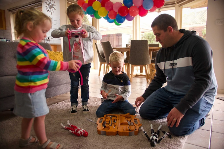 A man surrounded by three children in a lounge room