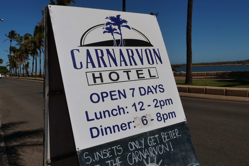 A Hotel sign in front of a bright blue sky and board walk with palm trees.