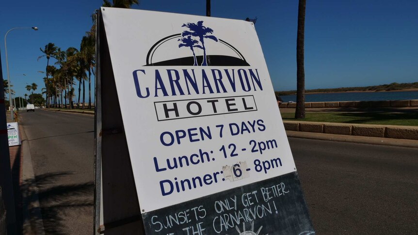 A Hotel sign in front of a bright blue sky and board walk with palm trees.