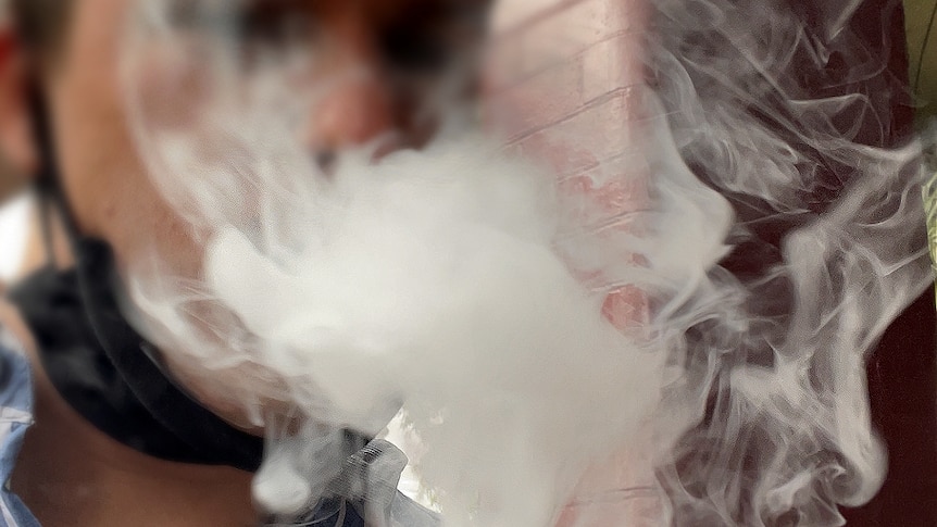 Vape clouds blur the face a person vaping with a mask around their neck