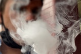 Vape clouds blur the face a person vaping with a mask around their neck