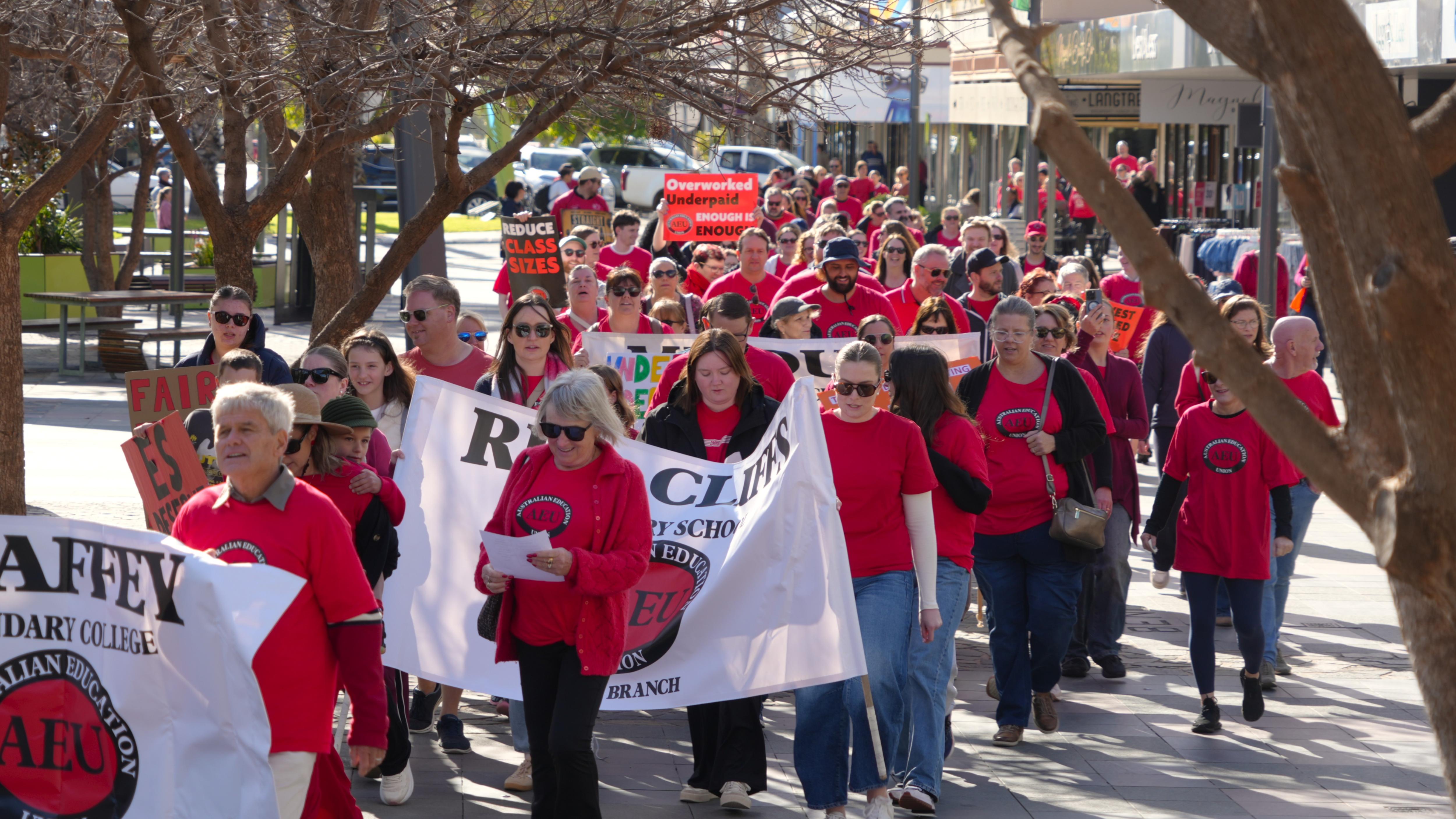 A large group of people in red shirts are marching along a green street.