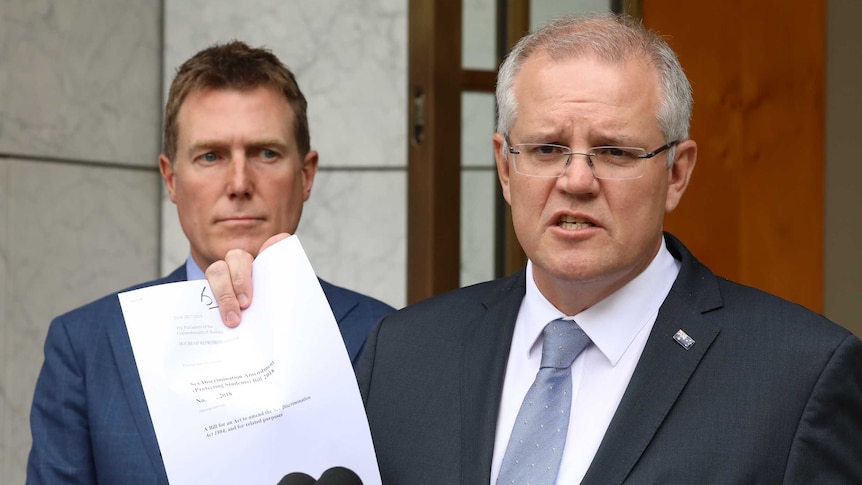 Mr Morrison is standing behind a lectern, holding up a copy of the bill. Attorney-General Christian Porter is behind him.