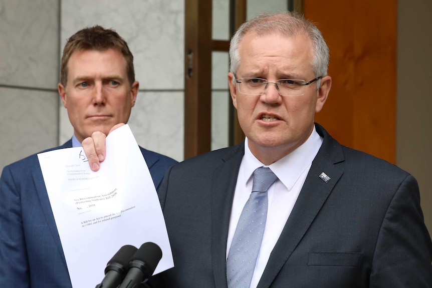 Mr Morrison is standing behind a lectern, holding up a copy of the bill. Attorney-General Christian Porter is behind him.