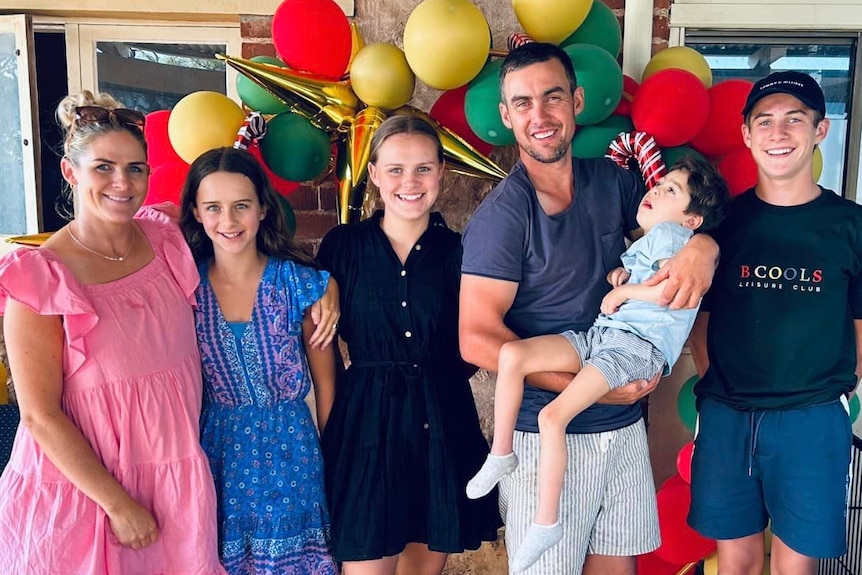 Two parents and their children in front of balloons, father holdng small boy