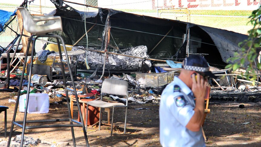 A police officer walks past the burnt out remains of the Aboriginal tent embassy in Musgrave Park.