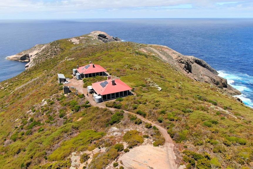 A drone shot of an island out to sea with two red-roofed cottages.