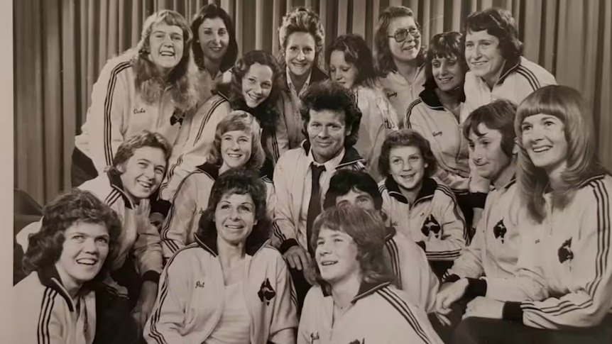 A women's soccer team wearing matching outfits pose for a photo with their head coach