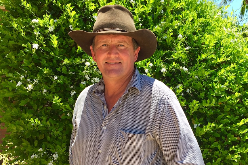 A man wearing a long sleeve button up shirt and akubra standing in front of a tree facing the camera.