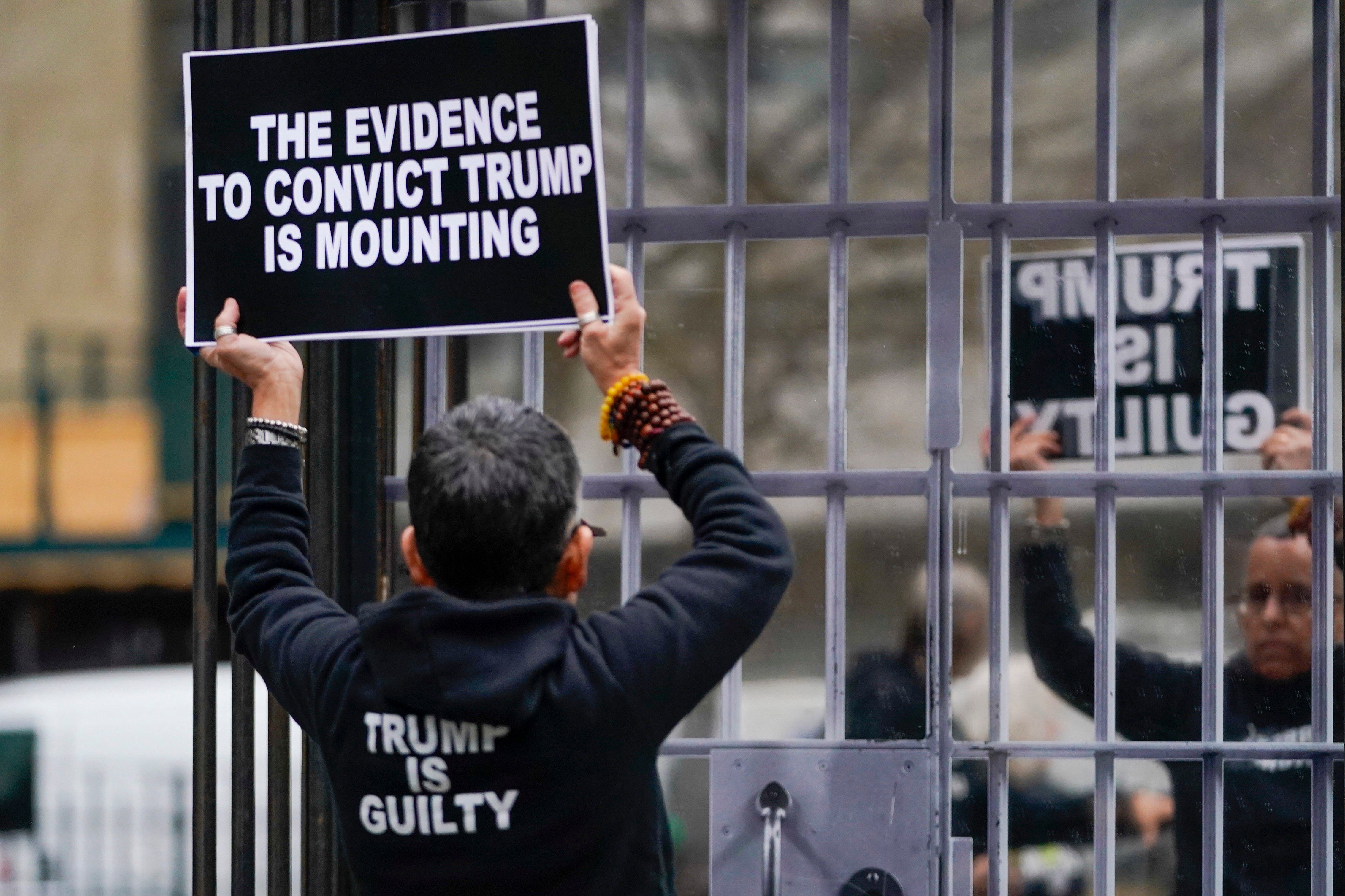 A person holds a sign that says: The evidence to convict Trump is mounting