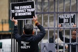 A person holds a sign that says: The evidence to convict Trump is mounting