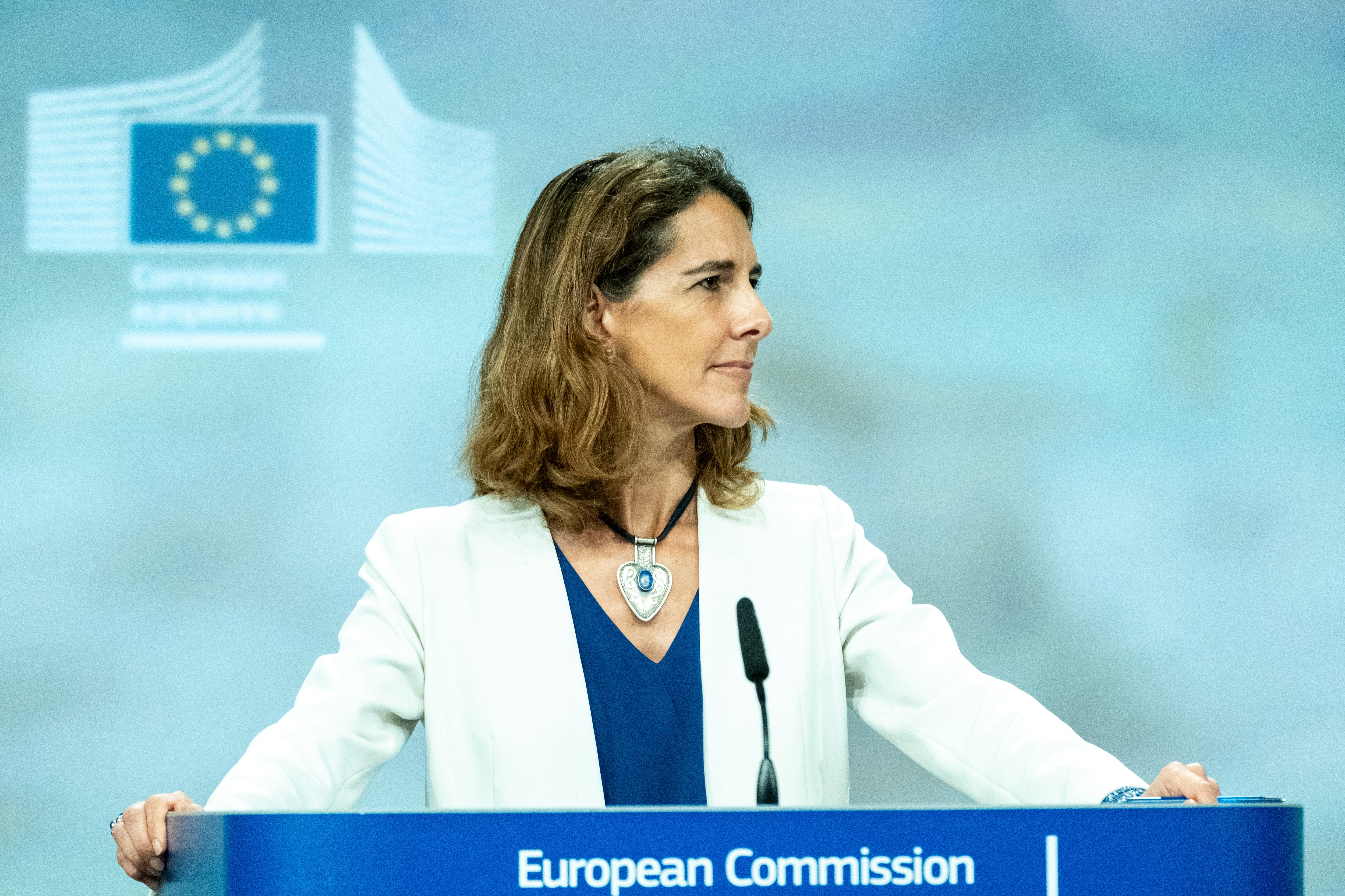 Uma mulher vestida com um fato branco e uma t-shirt azul, em frente a um stand da Comissão Europeia. 