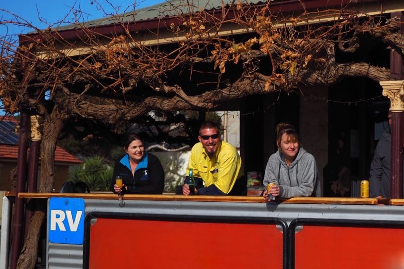 Six people stand along a pub's veranda, laughing and smiling.