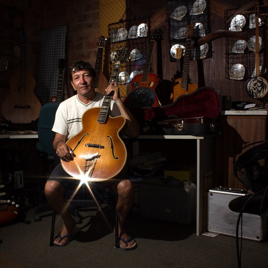 A man holding a guitar in a recording studio with shells on the wall.