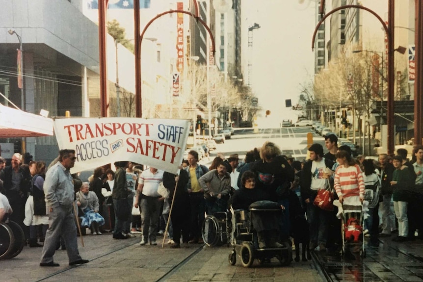 Protesters, both standing and in wheelchairs, prepare to march down a main street in Melbourne's CBD.