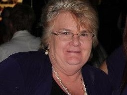 A middle-aged woman with short blond hair, wearing black, sitting at a table.