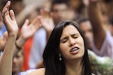 Woman praying, with hand held up and eyes closed, at Assembly of God church in Goiania, Brazil.