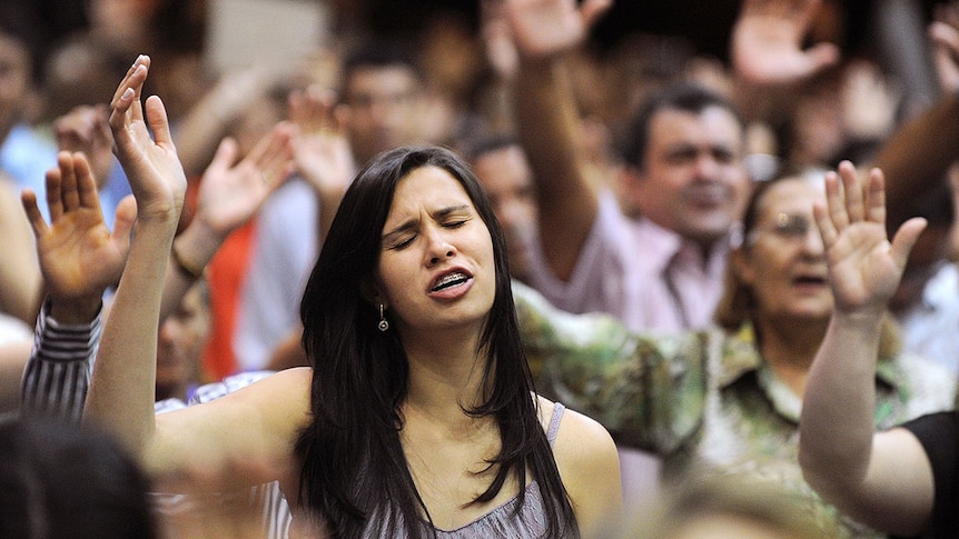 Woman praying, with hand held up and eyes closed, at Assembly of God church in Goiania, Brazil.