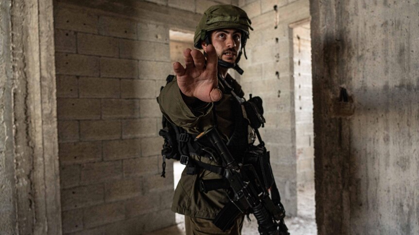 An Israeli soldier dressed in uniform and wearing a helmet holds up his hand to a journalist.