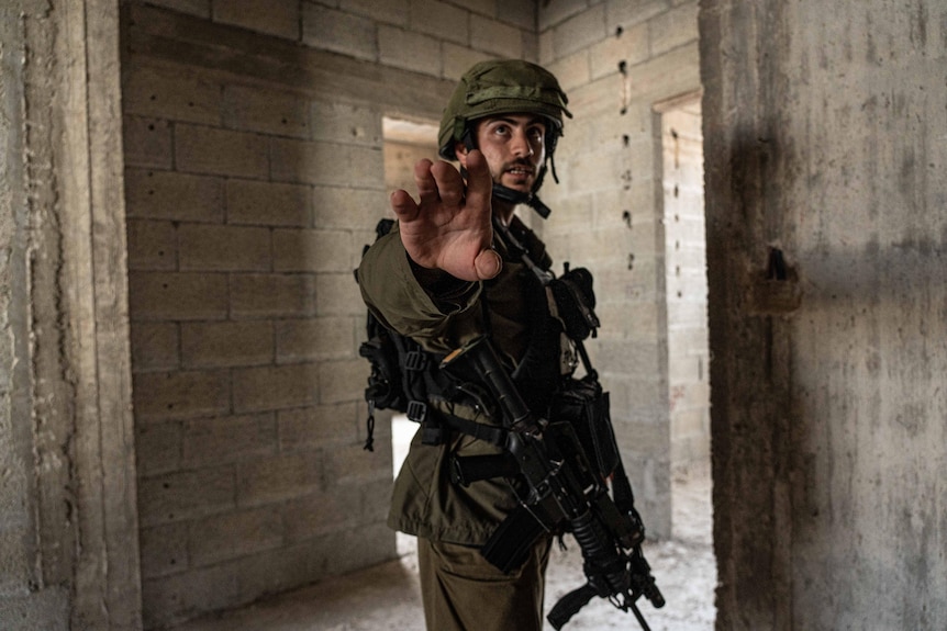 An Israeli soldier dressed in uniform and wearing a helmet holds up his hand to a journalist.