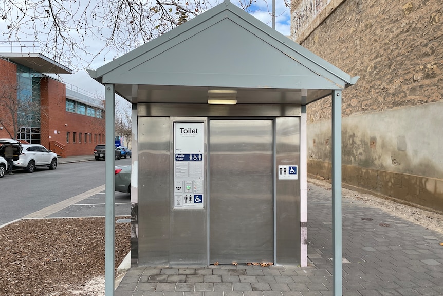 A silver public toilet block on a suburban street