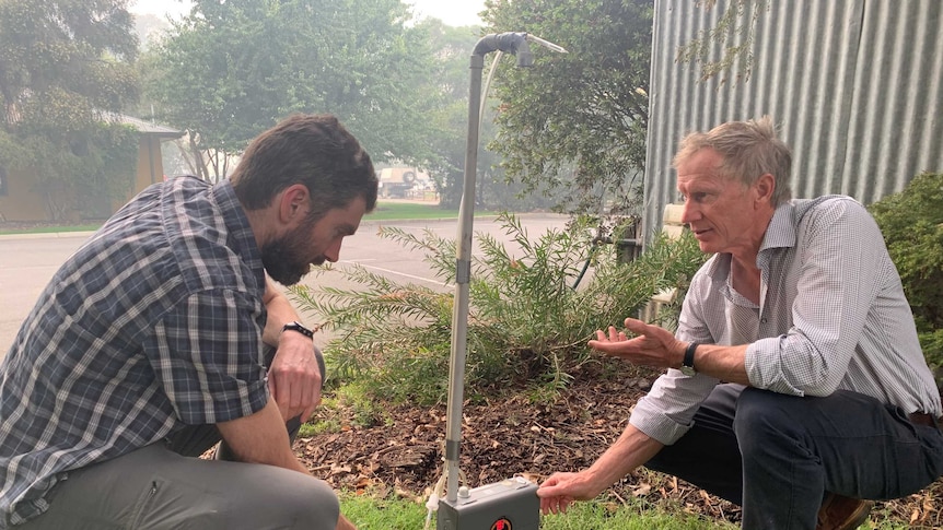 Two men examine a device on the ground which helps measure the smoke in the air.