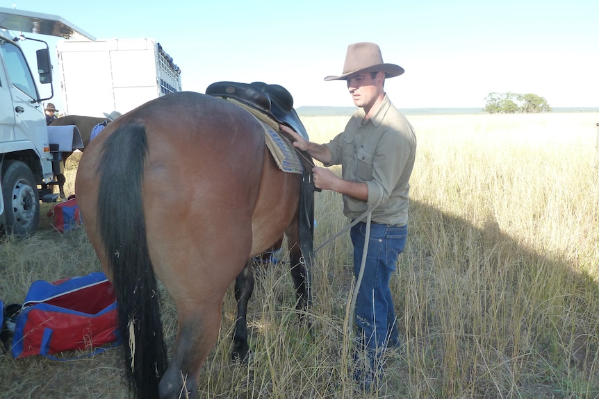 Detective Simon Jackson in a green shirt saddling up a horse in a paddock 