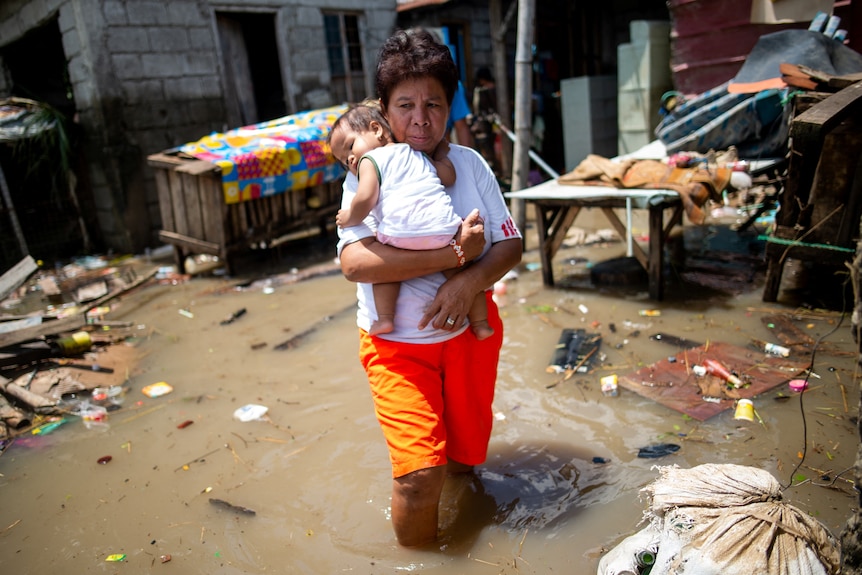 picture of a woman carrying a child and walking through flood water