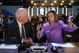 Nancy Pelosi sits at a desk with Ben Cardin, mid gesture. 