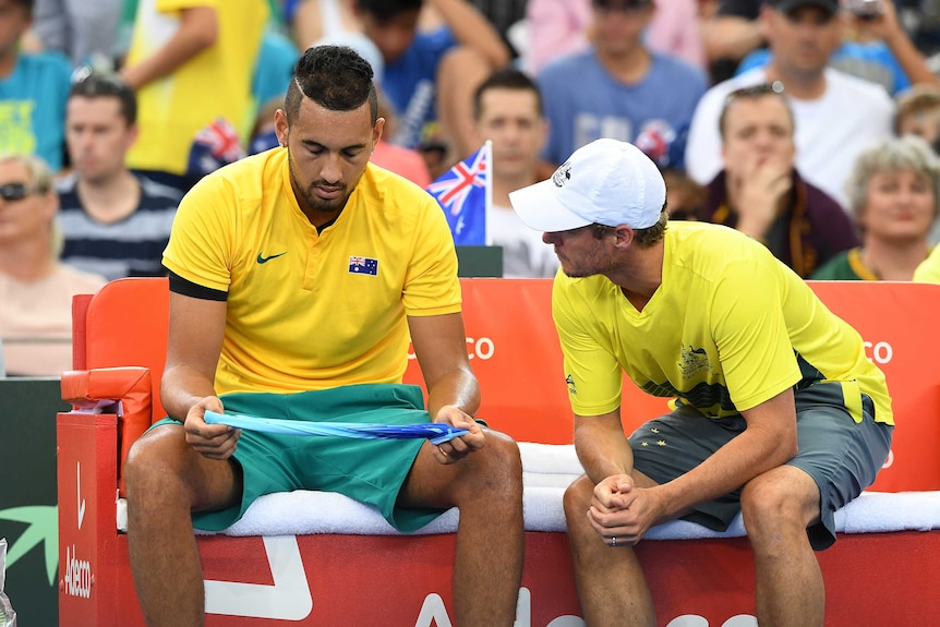 A national team coach speaks to a tennis player who is looking down at courtside.