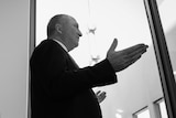 Barnaby Joyce in black and white from a low angle speaking at a press conference with his shadow on the wall behind him