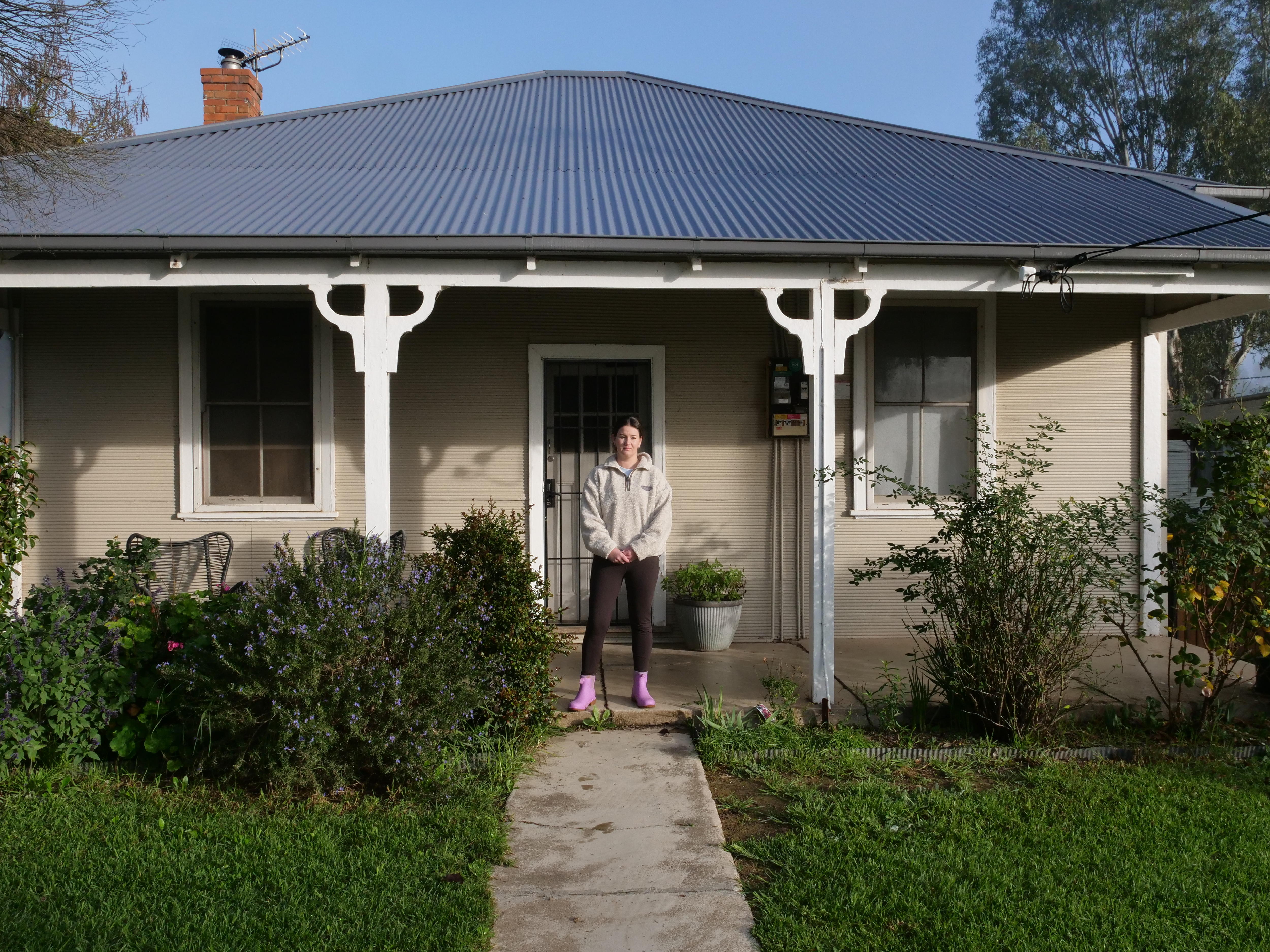woman in a tracksuit and gum boots stands in front of a house