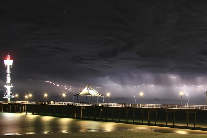 A black sky lit up by lightning strikes with a jetty in the foreground of the picture