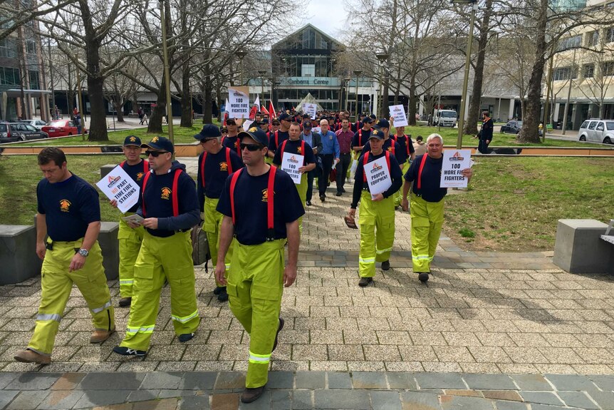 A group of ACT firefighters march together in Canberra, holding signs.