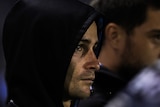 Halfback Nicho Hynes, with a hooded jumper over his head, sits on the bench and watches a match