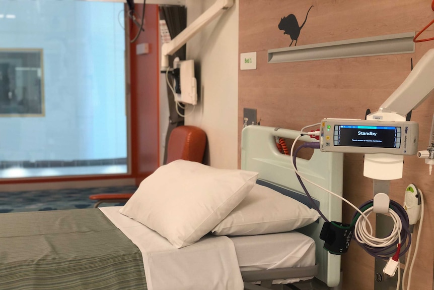 A fully made-up empty bed with medical equipment next to it in a ward at the Monash Medical Centre