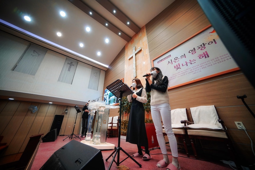 Two young Korean women singing into microphones in a church