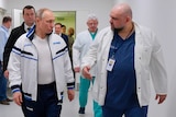 Vladimir Putin in a track suit walking down a hallway with a doctor