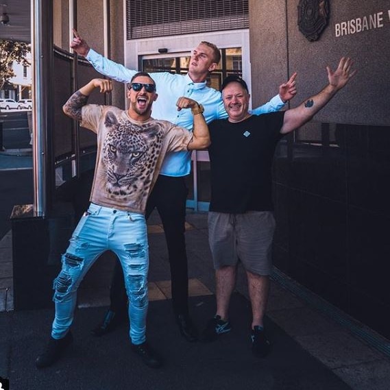 Luke Erwin (rear) with two others in front, with hands up in the air, posing, outside Brisbane watchhouse.