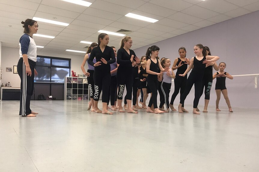 A group of young dance students happily following instructions from a teacher