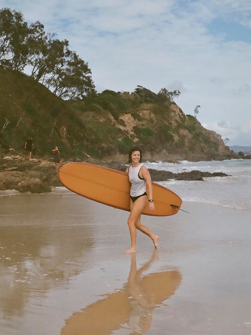 Female surfer walking up the beach with her board under her arm
